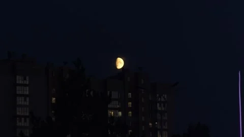A glowing half moon rising above dark city buildings at night. Stock Footage 343240849