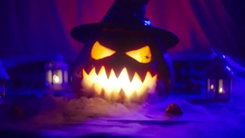 A glowing Halloween pumpkin wearing a hat with a carved grimace blowing smoke Vídeos de archivo 219286302