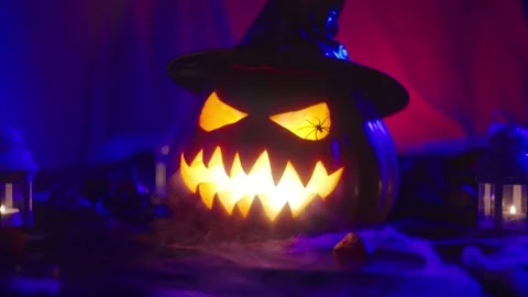 A glowing Halloween pumpkin wearing a hat with a carved grimace blowing smoke Видео 221787723