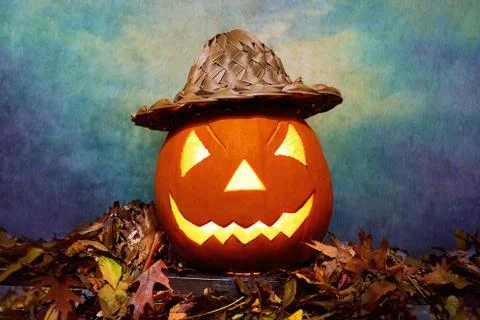 Glowing Halloween pumpkin in wicker hat on heap of leaves Stock Photos