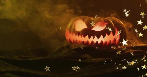 Glowing jack-o'-lantern casting glow in studio on drape with smoke, gold star Stock Photos