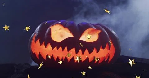 Glowing jack-o'-lantern casting orange light on rock at night, with blue-gray Stock Photos