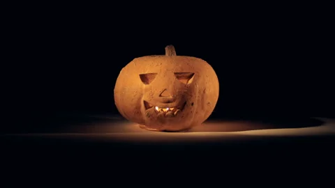 Glowing jack-o-lantern standing on a surface in a dark room Video stock 95583468