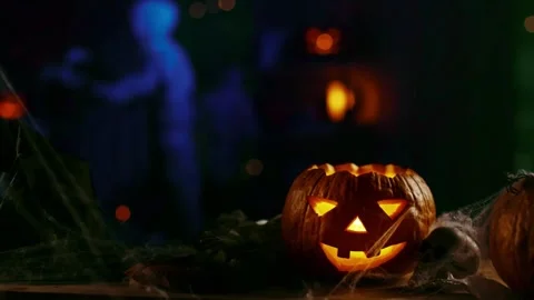 Glowing jack o lantern on table with blurred zombie walking in background. Stock Footage 346723185