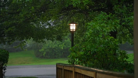 Glowing lantern in heavy rain over a wooden deck and residential street Stockbeeldmateriaal 320920482