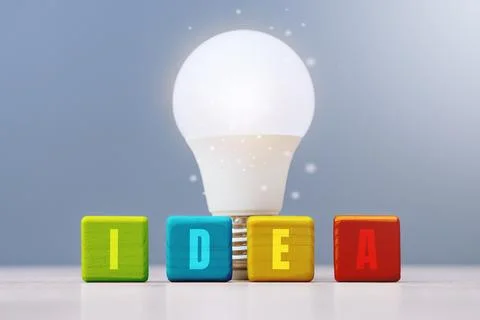 Glowing LED light bulb stands behind colorful wooden cubes spelling the word  Stockfoto's