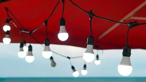Glowing LED string lights suspended under a red canopy outdoors at twilight. Stock Photos