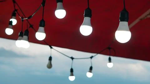 Glowing LED string lights suspended under a red canopy outdoors at twilight. Stock Photos