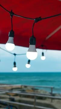 Glowing LED string lights suspended under a red canopy outdoors at twilight. Stock Photos