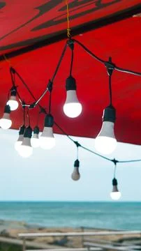 Glowing LED string lights suspended under a red canopy outdoors at twilight. Stock Photos