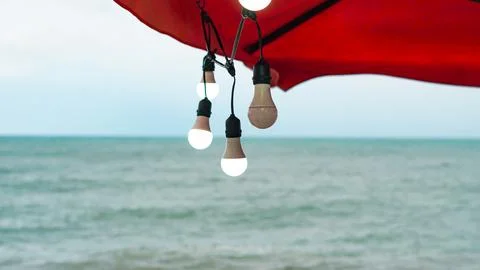 Glowing LED string lights suspended under a red canopy outdoors at twilight. Stock Photos