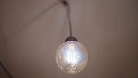 Glowing light bulb closeup showing filament and glass texture with soft indoor Stock Footage 346729442