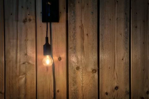 Glowing light bulb hanging near wooden panaled wall background texture, modern Stock Photos