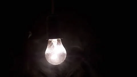 Glowing Light Bulb Hanging in Thick Smoke on a Black Background in Empty Space Stock Footage 262783098