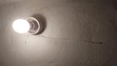 Glowing light bulb on a textured ceiling with a long spider web hanging across t Stock Footage 335474899