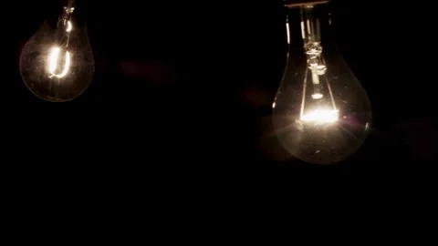 Glowing light bulbs swing slowly against a dark background Stock Footage 329666945