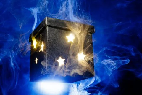 Glowing magic box with star cutouts and blue smoke on dark background Stock Photos