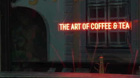 Glowing neon coffee and tea sign in shop window with reflective facade, warm Stock Footage 337735656