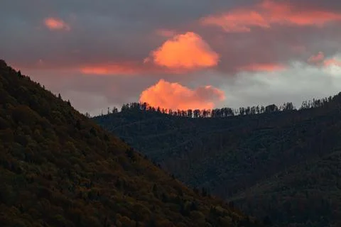 Glowing Orange Cloud Above Dark Forested Mountain Peak at Sunset Stock Photos