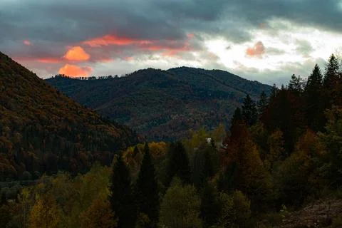 Glowing Orange Cloud Above Dark Forested Mountain Peak at Sunset Stock Photos