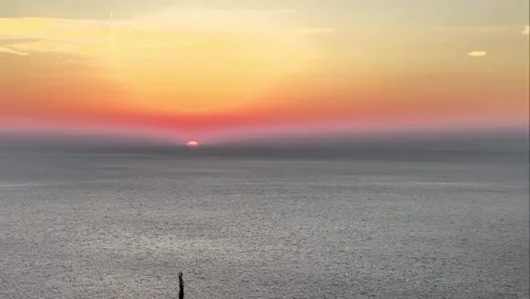 Glowing Orange Sunset Over Calm Ocean and Hilly Coastline Vidéo 339880744