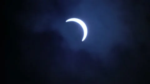 Glowing Partial Solar eclipse crescent, on a cloudy, dark blue sky Stock Footage 145444366