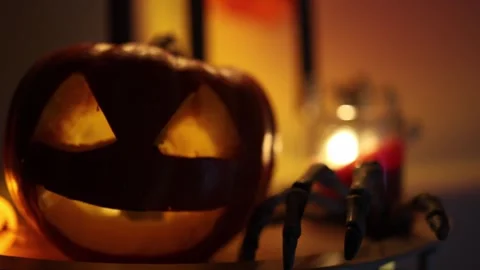 Glowing pumpkin and skeleton hand create an eerie Halloween home atmosphere Stock Footage 346147158