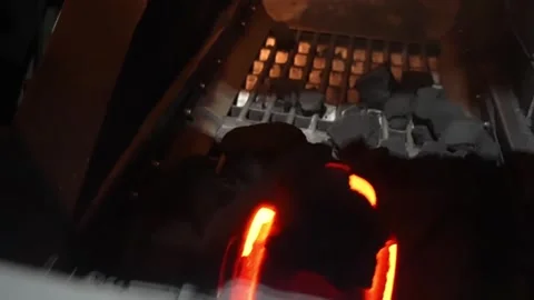 Glowing red-hot castings visible inside sand molds on shakeout conveyor at Stock Footage 336632245