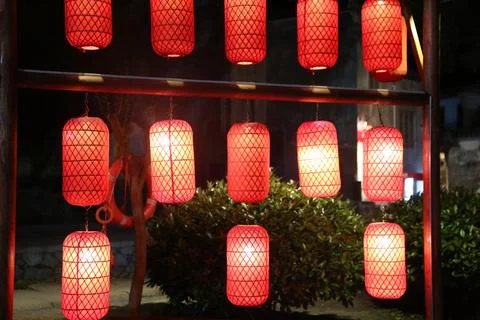 Glowing red lanterns hanging in rows from a wooden frame in a dark outdoor .. Stock Photos