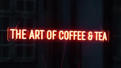 Glowing red neon coffee and tea sign hanging in dark interior, creating warm Stock Footage 337735699
