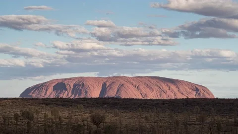 Glowing red Uluru under passing clouds time lapse at sunset time 8k Stock Footage 131406538