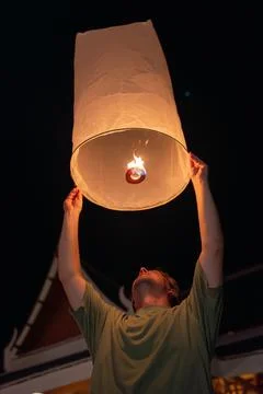 Glowing sky lantern release at night with warm flame inside, upward gaze and Stock Photos