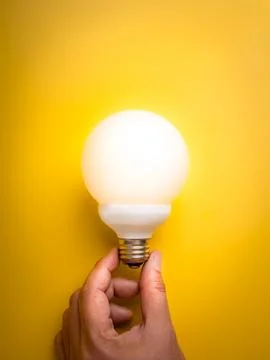 Glowing sphere light bulb held by hand on yellow background. New idea, crea.. Stock Photos