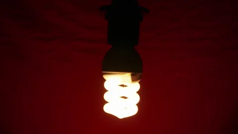Glowing Spiral Light Bulb Illuminating Against Dark Red Background Vídeos de archivo 334134095