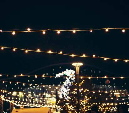 Glowing string lights, dark night sky in city, winter holidays, blurry Christmas Stock Photos