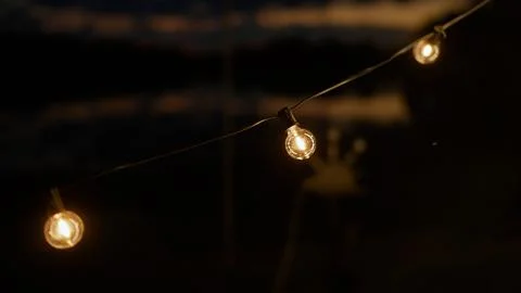 Glowing string lights with warm yellow bulbs hanging outdoors against dark 스톡 사진