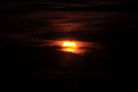 Glowing sun behind dark clouds at sunset Stock Photos