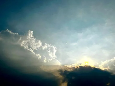 Glowing sun shining through dark clouds in dramatic blue sky during sunsite Stock-Fotos
