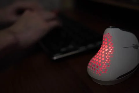 A glowing vertical computer mouse against the background of a programmer's .. 스톡 사진
