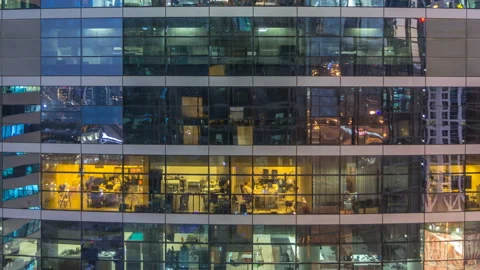 Glowing windows in multistory modern glass and metal office building light up at Stock Footage 100659976