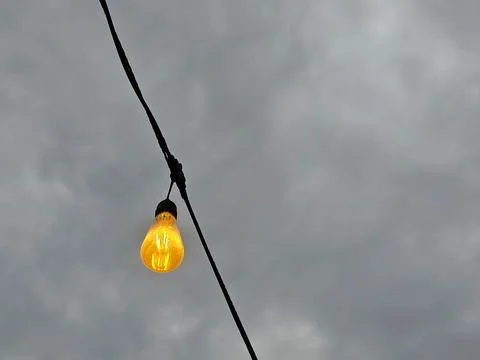 Glowing yellow string lights against a dark cloudy sky Stock Photos