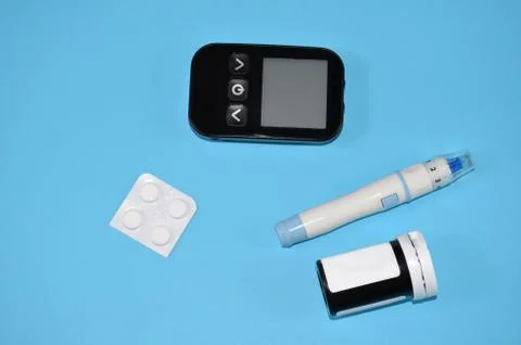 Glucometer and pills on a blue background. Stock Photos