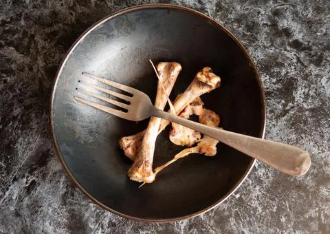 Gnawed chicken bones and a fork in a plate Stock Photos