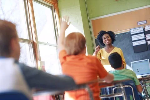 Go ahead and answer. a young boy raising his hand to answer his teachers Stock Photos