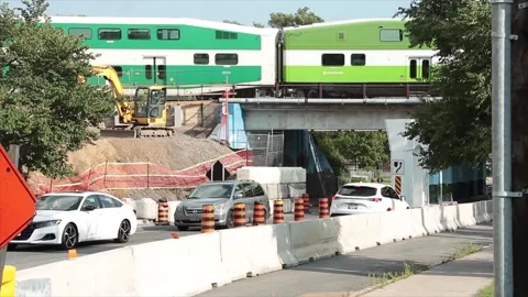 Go train passing on overpass bridge above construction traffic cars vehicles Stock Footage 249420650
