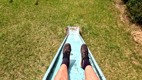 Going down an old and worn slide located in a playground for children Stock Footage 336872209