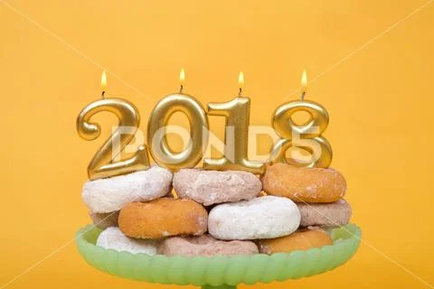 Gold 2018 number candles burning brightly on top of a pile of donuts sitting Stock Photos