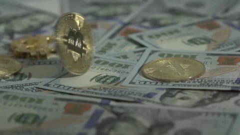Gold bitcoin BTC rotate in on the table with many 100 dollars bills and another Stock Footage 129802985