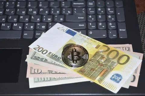 A gold Bitcoin coin and a stack of euro bills lie on a laptop keyboard Stock Photos