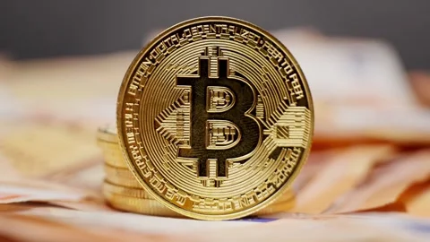 Gold Bitcoin coin on a stack of coins with euro bills underneath representing Stock Footage 312604539